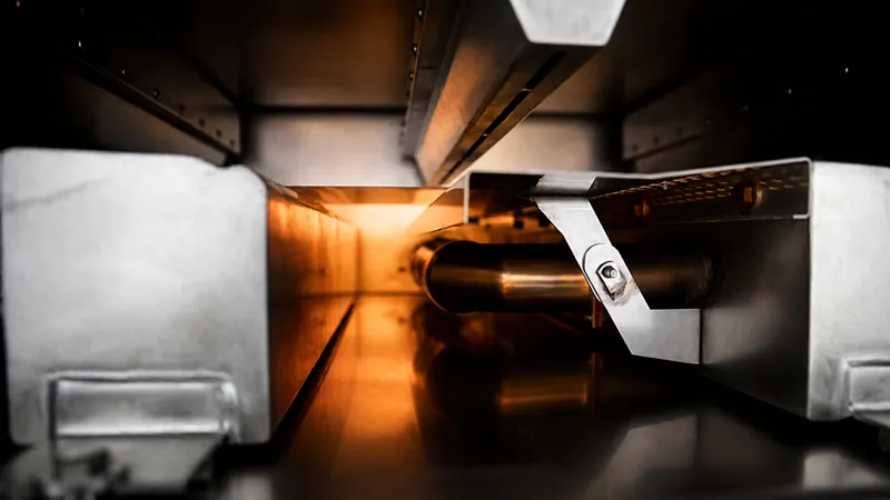 Interior view of an industrial curing oven with a metal conveyor roller under warm orange heating light