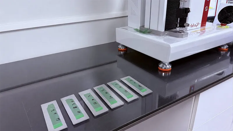 Prepared release liner test strips arranged beside a tester for multi-property evaluation